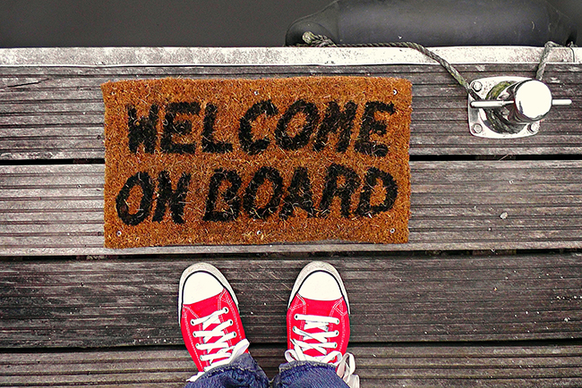 Feet next to "Welcome On Board" mat — onboard and train new volunteers