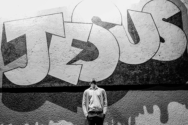 man looking up at graffiti art spelling "Jesus" - what do we believe about Jesus?