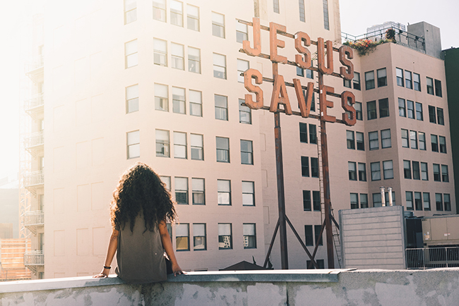 Woman sitting on wall looking at "Jesus Saves" sign - importance of church