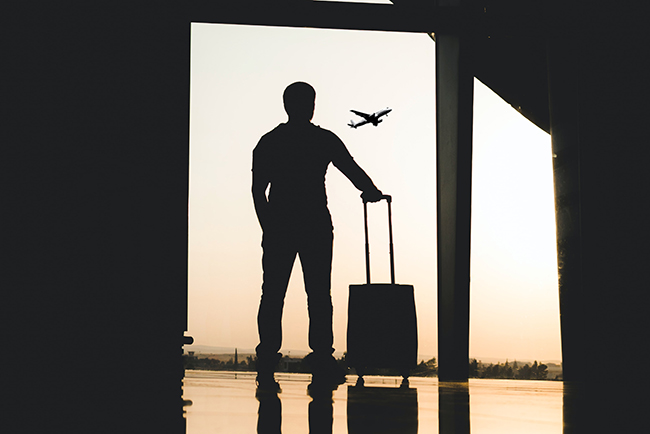 Silhouette of man standing with luggage, watching airplane take off - Immigration