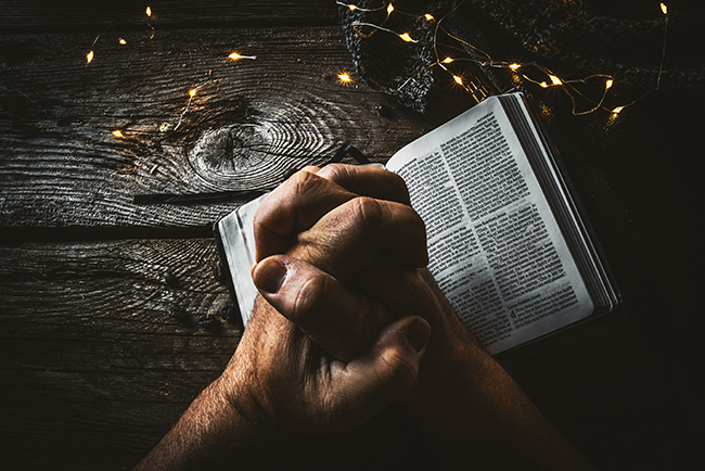 man's hands folded in prayer over open Bible - Half of Americans believe in God