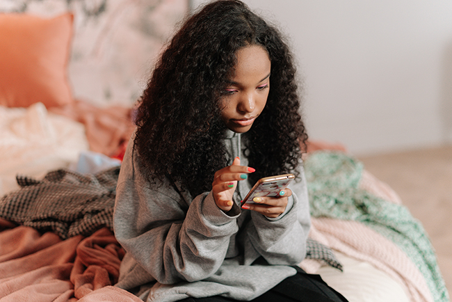 teenage girl sitting on bed using cell phone - the next generation is leaving the faith