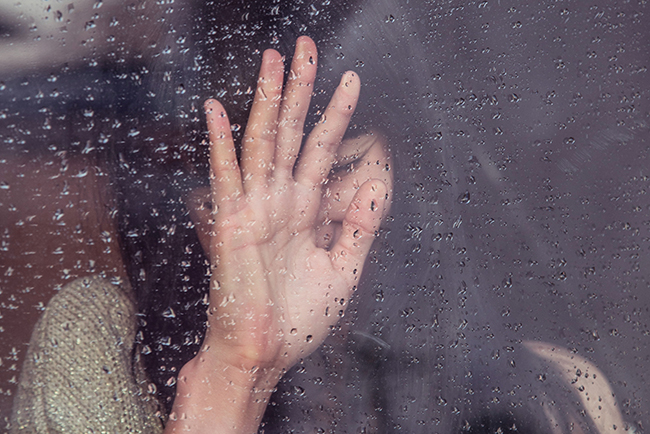 Woman touching rainy glass window - domestic violence awareness