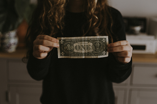 Woman holding dollar bill in front of her - economy impact on churches