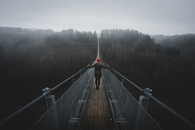 Woman walking across long suspension bridge - taking the edge off fear by trusting in God