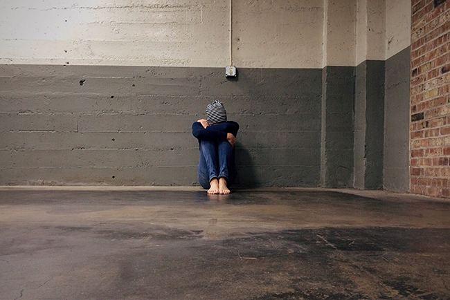 Person sitting against wall with head between knees - tackling human trafficking