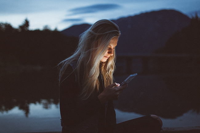 Woman looking at phone near the lake in the evening - online Bible reading