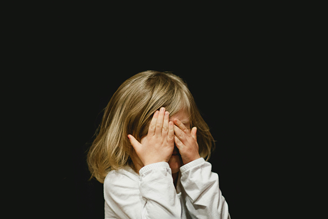 Small girl covering her face in front of black background - support children who've experienced trauma
