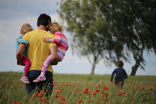 Man carrying kids through field of flowers - cost of having children