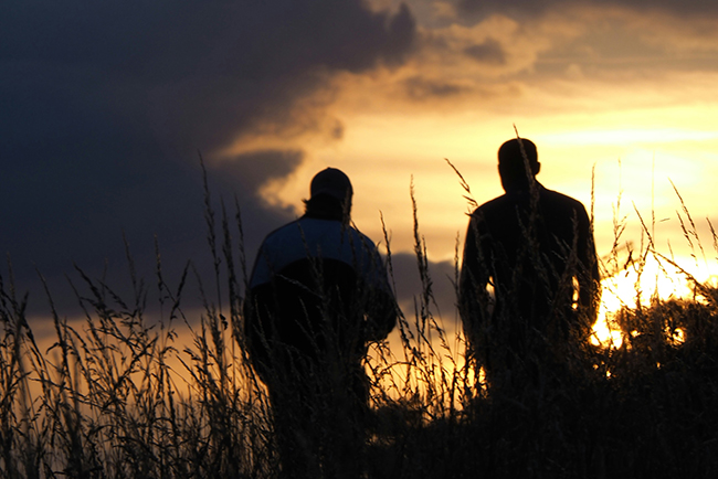 silhouette of two men standing in field at sunset- investing in men