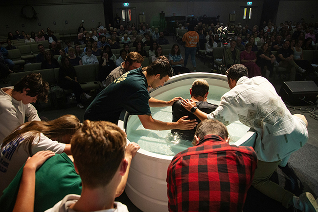 People praying around young man getting baptized - baptism